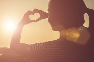 young woman hands shaped heart against beautiful sunset.